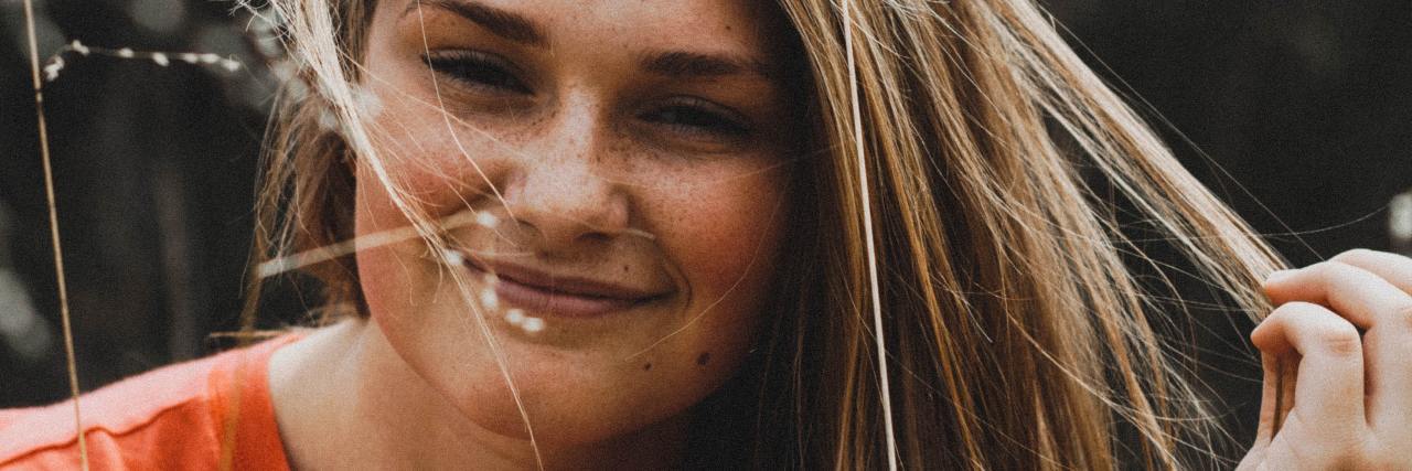 A Therapist's Guide To Mental Health Self-Care During COVID-19 photo of young woman smiling for camera with hand in her hair