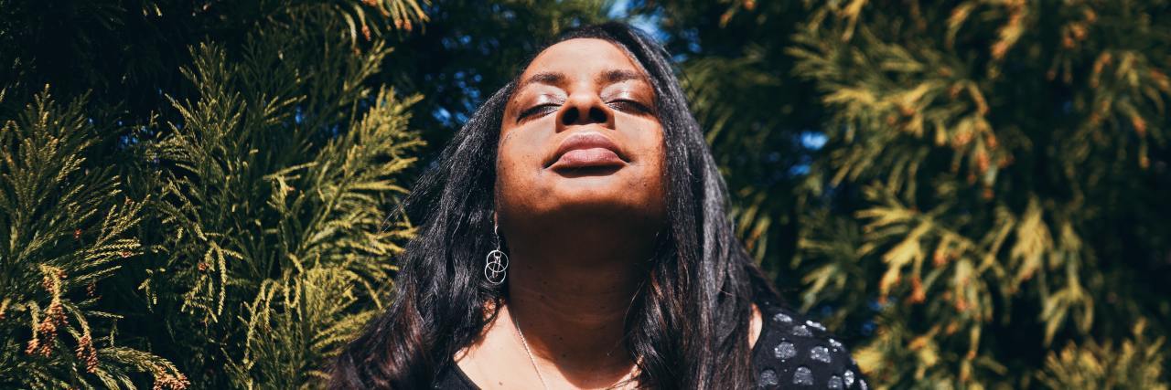 Tips for Effectively Managing PTSD Flashbacks photo of woman with her eyes closed and face raised to sunlight with trees behind her