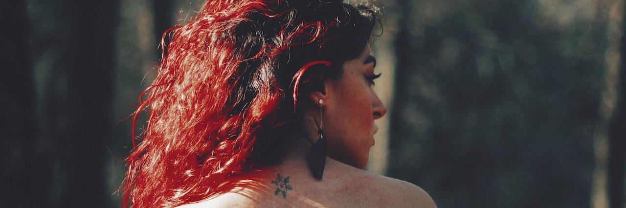 Can PTSD Be a Cause of Impulsive or Reactive Behaviors? Woman with curly red hair wearing a black, sleeveless shirt look over one shoulder