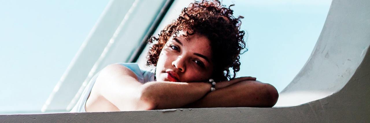 Can PTSD Cause Anhedonia or Loss of Pleasure? Sad-looking woman with curly brown hair resting her head on her arms in front of a window