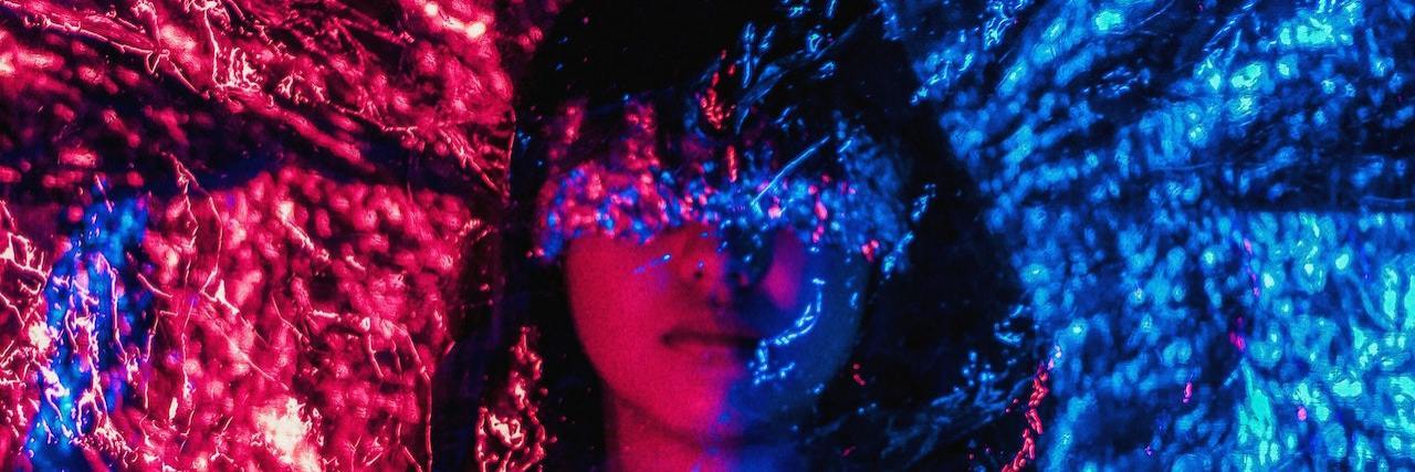 Can Depersonalization Be a Symptom of PTSD? Woman with dark hair blending into a blue and red abstract background