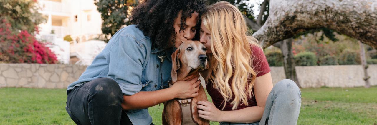 How to Solve Relationship Problems in COVID-19 Lockdown photo of a queer couple, one Black woman and one white woman, each kissing a dog outdoors