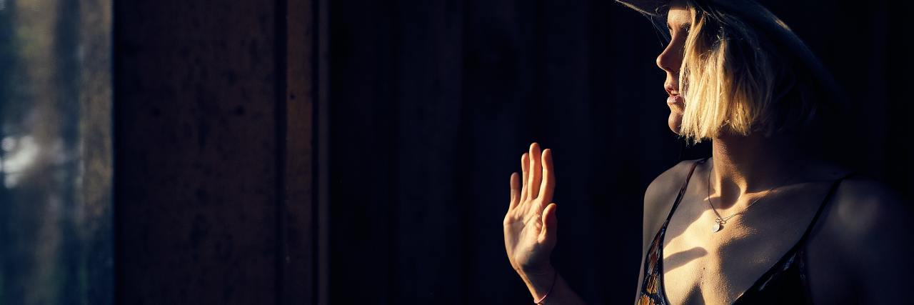 photo of woman holding up her hand in darkness, illuminated by light through window