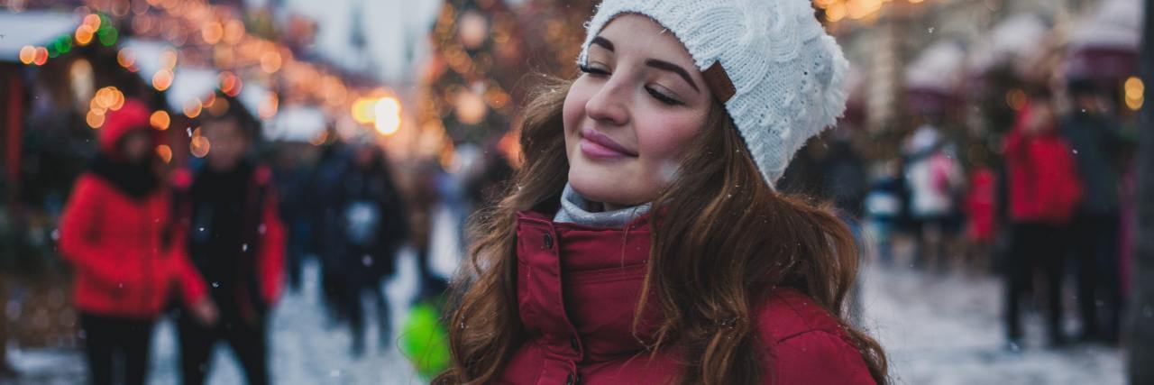 How Planning Everything Helps My Anxiety During the Holidays photo of woman in winter with christmas tree behind her, smiling with her eyes closed