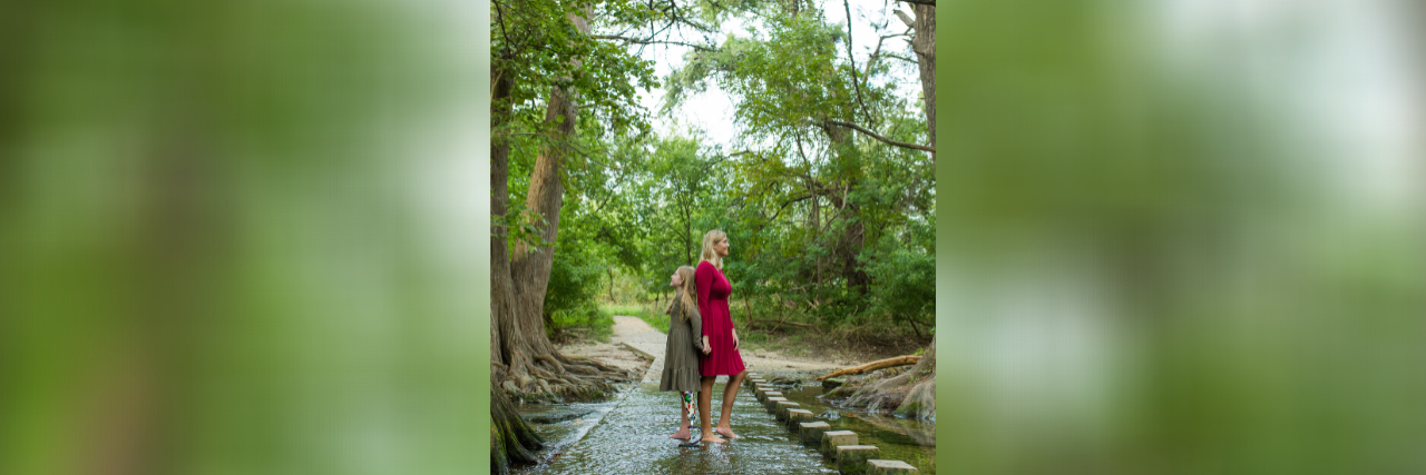 Coping With COVID-19 by Staying Positive and Choosing Joy Photo of contributor and her daughter standing in shallow water with backs together, surrounded by beautiful trees