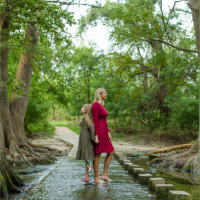 Photo of contributor and her daughter standing in shallow water with backs together, surrounded by beautiful trees