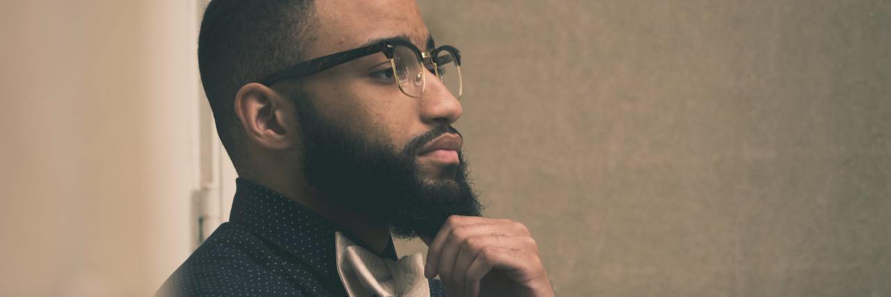 How To Cope With Anxiety and Election Uncertainty photo of man with a beard and glasses, leaning against wall with hand raised to beard, thinking