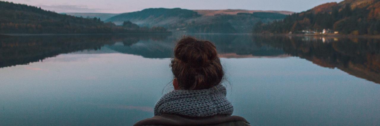 photo of woman from behind looking at still water of reservior