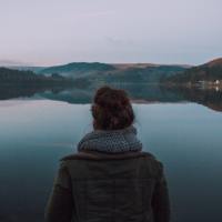 photo of woman from behind looking at still water of reservior