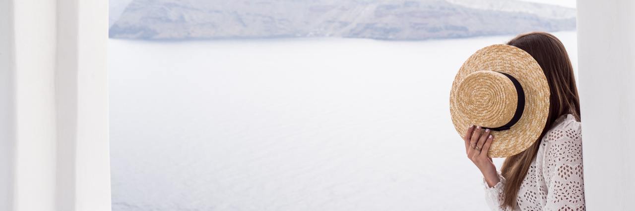 How Fibromyalgia Leaves Me Lonely and Exhausted woman looking out into an ocean, covering her face with a sunhat
