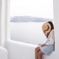 woman looking out into an ocean, covering her face with a sunhat