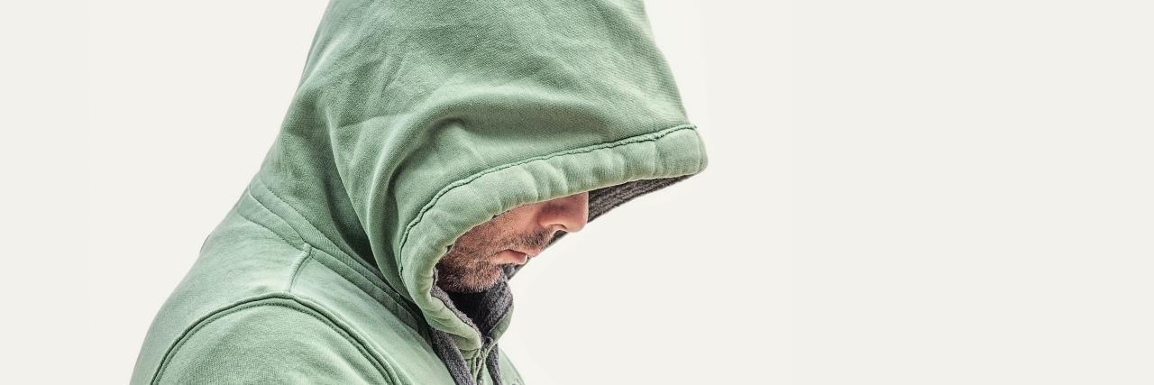 Why Childhood Trauma Makes Me Freeze in Arguments photo of man in hooded sweatshirt and profile view, face partly hidden with his head down and sad expression