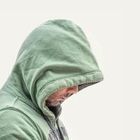 photo of man in hooded sweatshirt and profile view, face partly hidden with his head down and sad expression