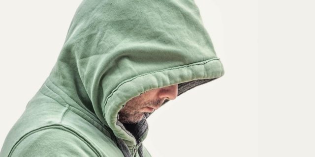 Why Childhood Trauma Makes Me Freeze in Arguments photo of man in hooded sweatshirt and profile view, face partly hidden with his head down and sad expression