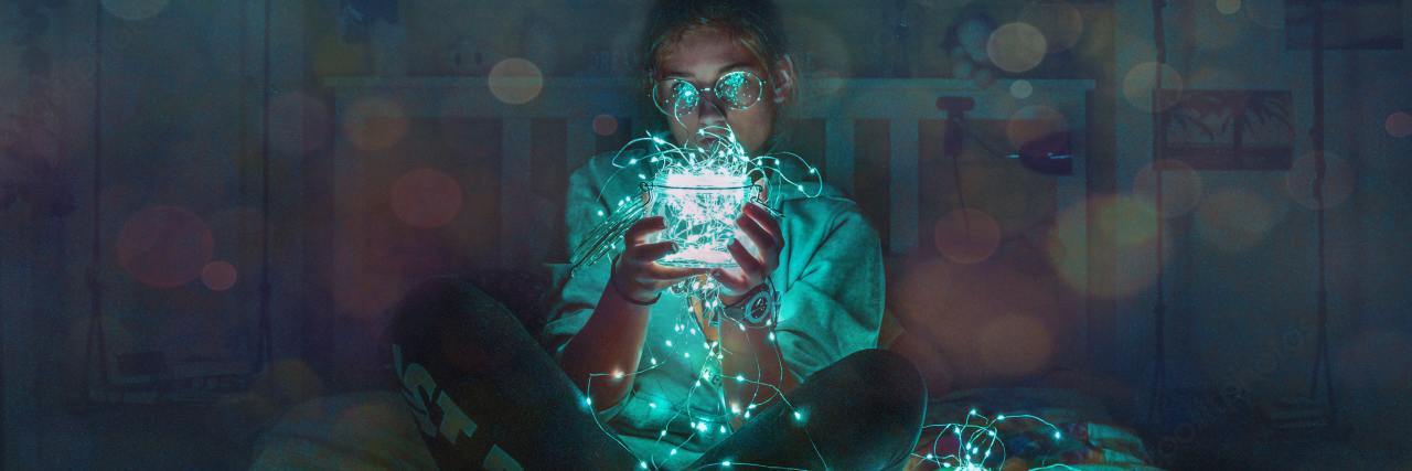 Mental Health 'Permission Slips' to Help Get You Through a Hard Time photo of woman sitting on bed with blue LED string lights in a jar and around her, holding it close to her face