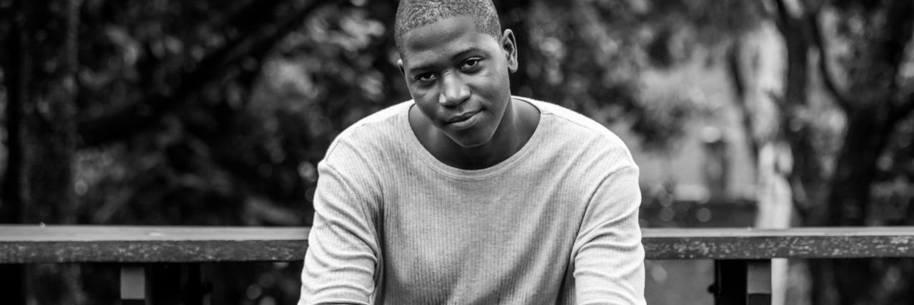 World Kindness Day: Self-Love Reminders as a Disabled Black Trans Man photo of man in black and white, sitting on a bench and smiling into camera