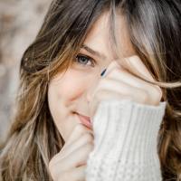 photo of woman looking into camera, covering face and smiling, looking shy