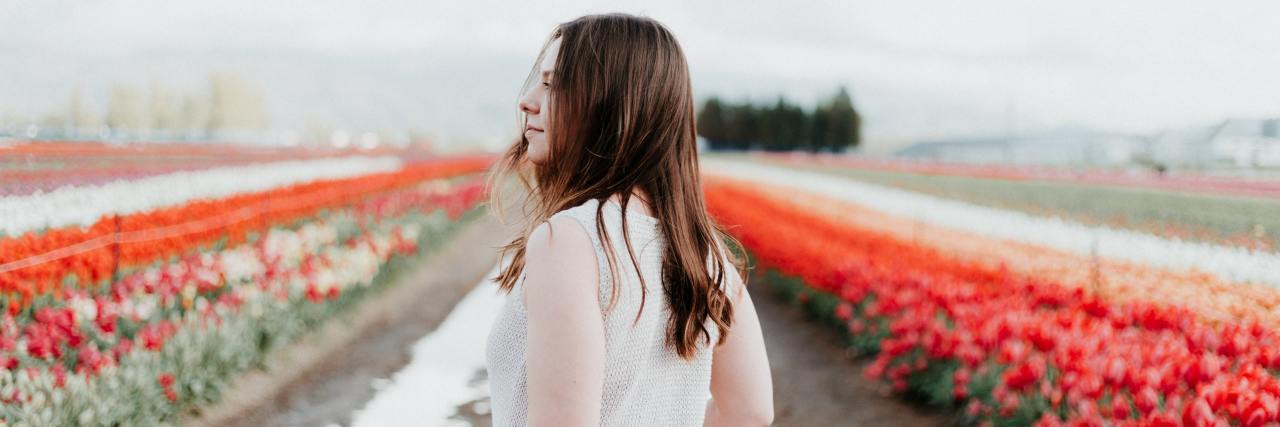 photo of woman standing in field of flowers facing away from camera