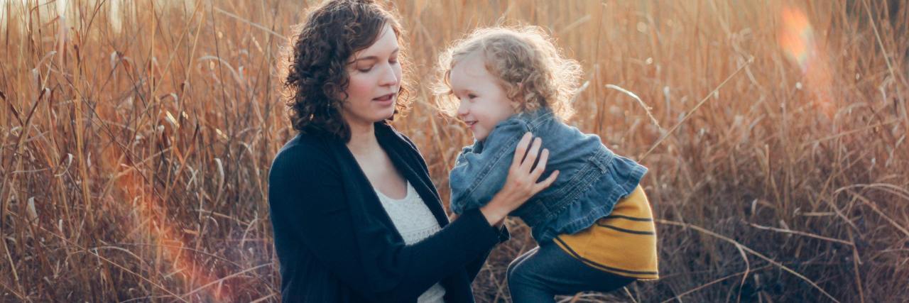 Read This if Your Mental Health Is Affected by Being 'Just a Mom' photo of woman holding young smiling girl or daughter in a field