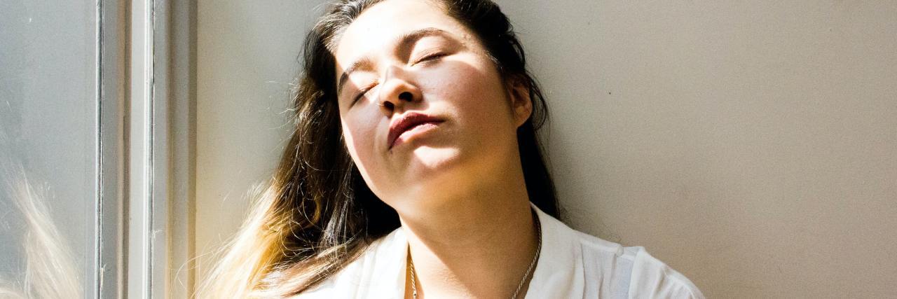 Experiencing Lack of Motivation With Schizphrenia photo of woman resting against wall by window with her eyes closed