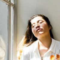 photo of woman resting against wall by window with her eyes closed