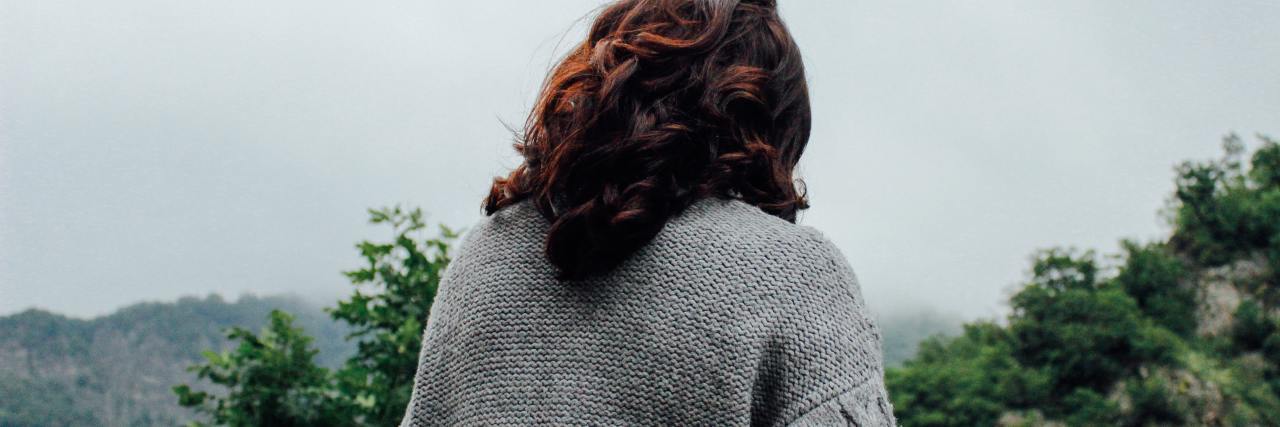 How You Can Be 'Privileged' About Your Mental Health photo of woman in white cardigan taken from behind, looking down with trees in background