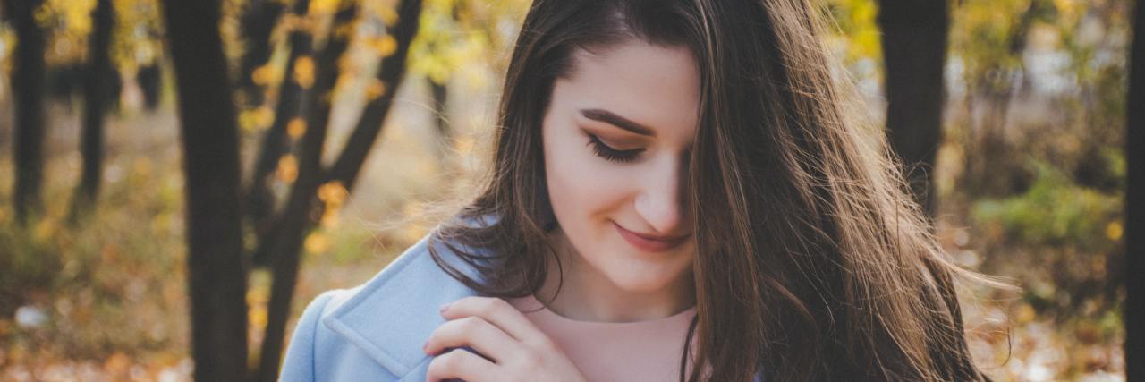 Using The Phrase 'Well Yeah, But' to Find Gratitude in Depression white woman with long brown hair outside during fall looking down, smiling to herself