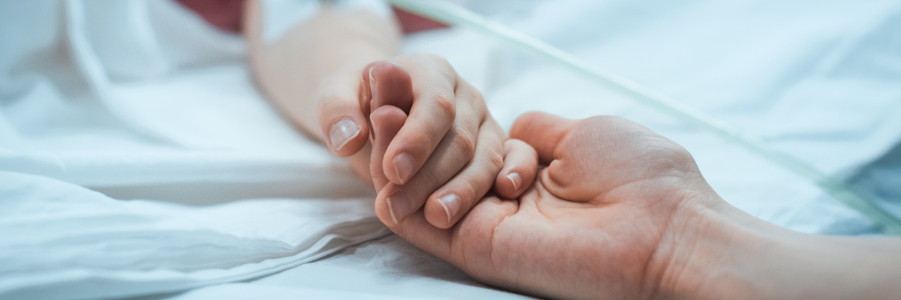 Man holds woman's hands as she recovers in hospital bed