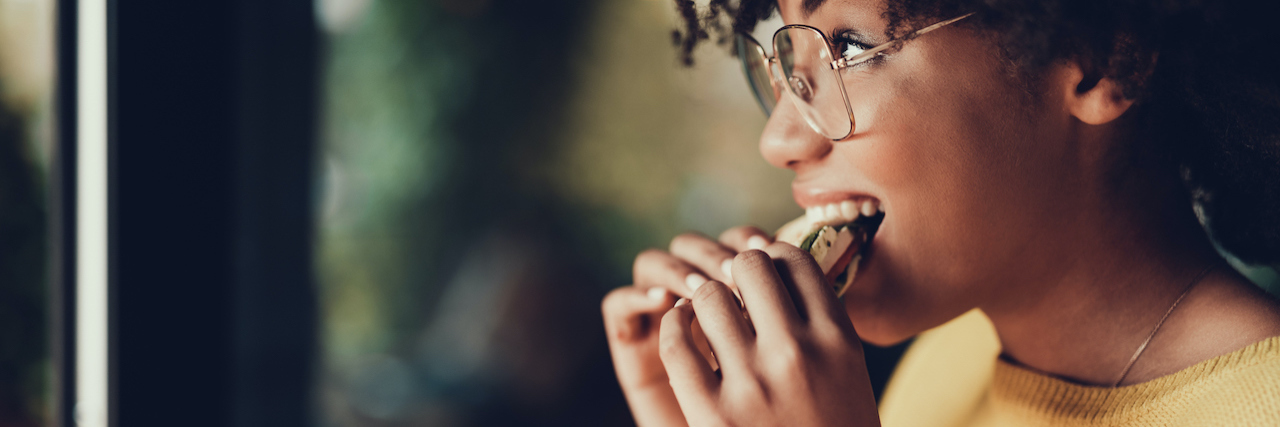 What Kaiser Permanente Got Wrong About Intuitive Eating A woman eating a sandwich at a restaurant, smiling