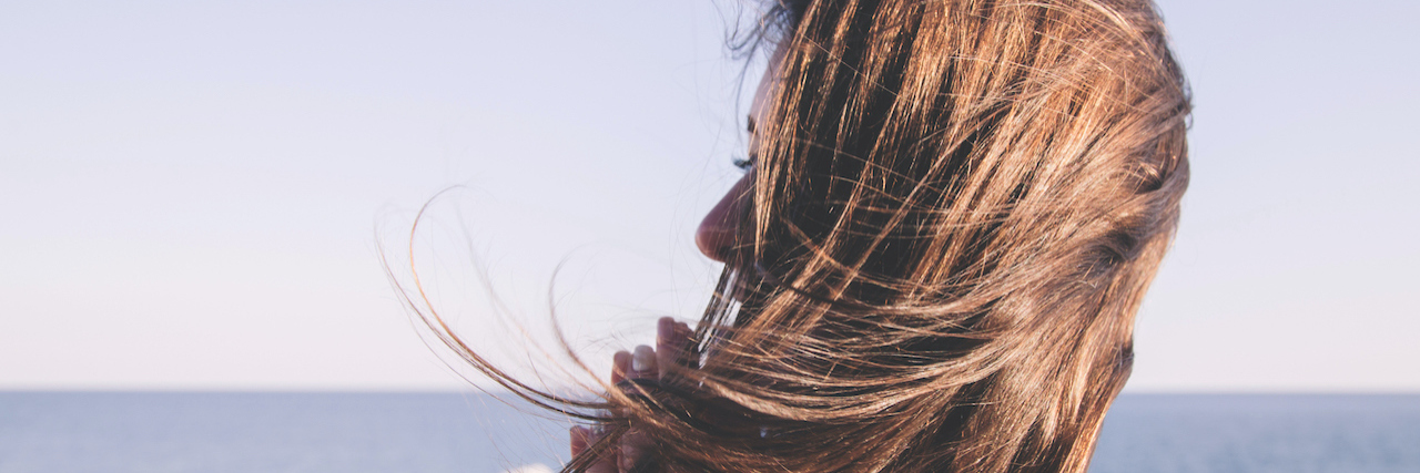The Problem of Delaying Chronic Illness Treatment During the Pandemic Woman with dark hair stands on a windy cliff over blue sea