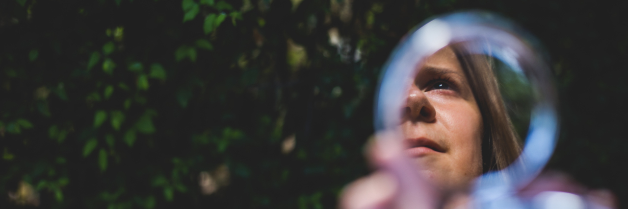 The Toxic Myths I Internalized as a Person With Facial Differences Woman’s face reflecting in small round mirror.