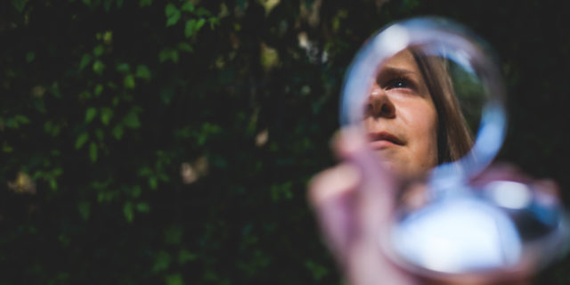 Woman’s face reflecting in small round mirror.