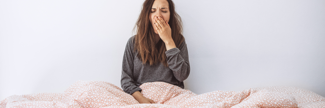 photo of young woman in bed tired and yawning, hand covering mouth