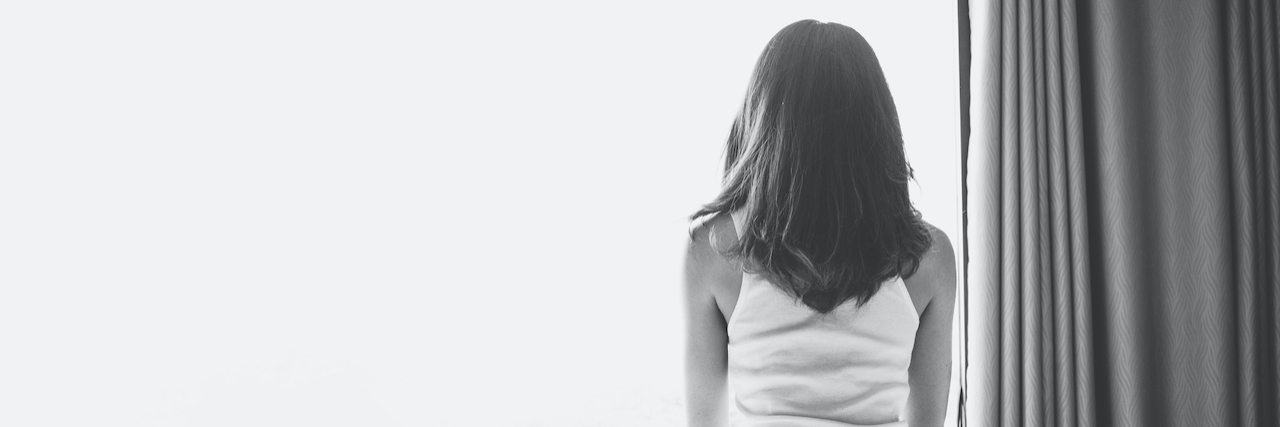 Black and white photo of the back of a woman sitting on a bed