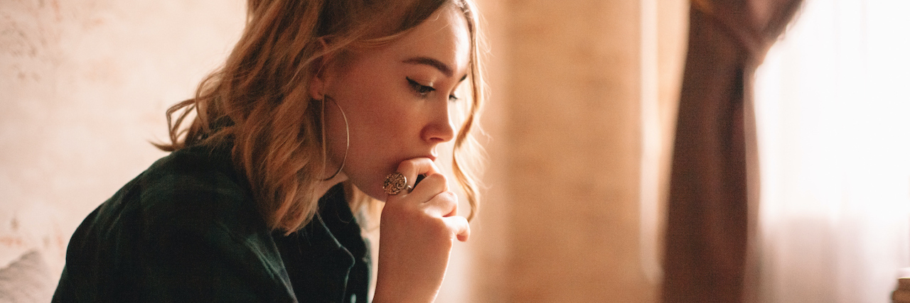 I Can't Have Kids Because of Ehlers-Danlos Syndrome A woman looking serious, sitting on a couch drinking tea.