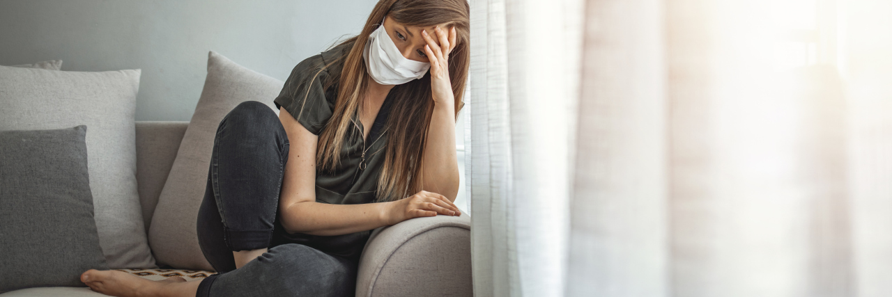 photo of woman looking upset or tired while indoors beside window and wearing coronavirus face mask