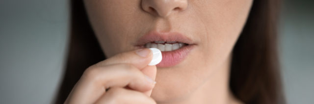 photo of a woman raising a pill to her lips, close up