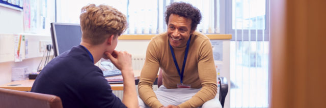 male counselor smiling, talking to a student across from him