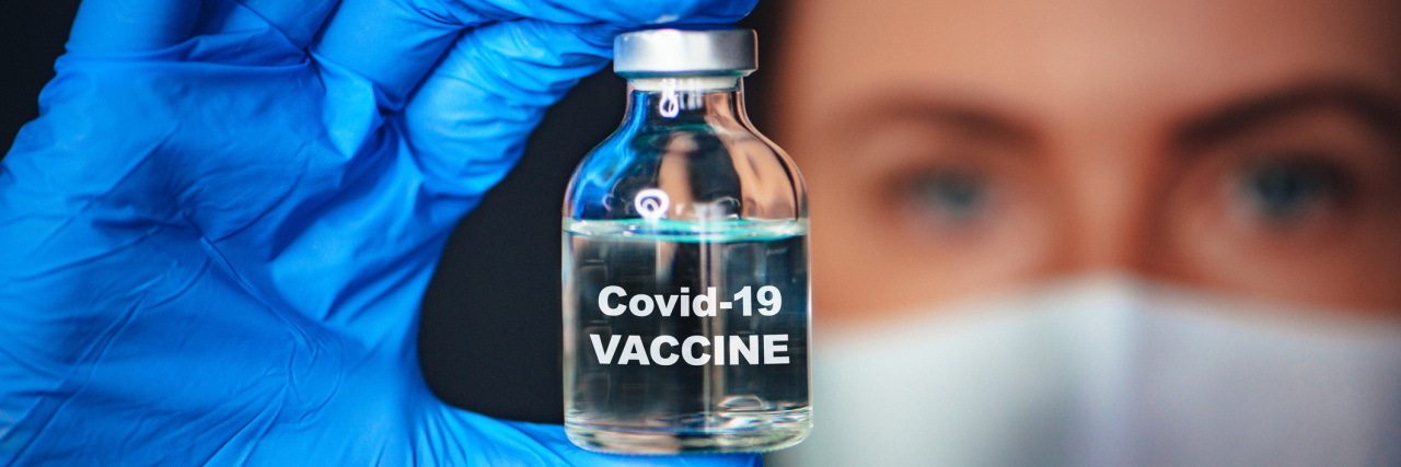 doctor wearing a mask with a bottle of covid vaccine