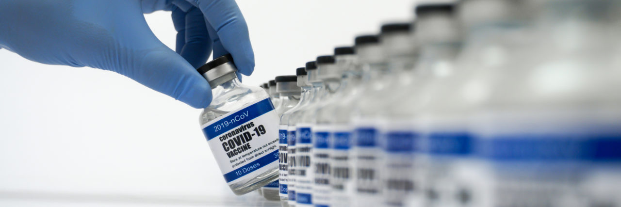 Blue gloved hand pulling a vaccine bottle out of a long line of vaccine bottles