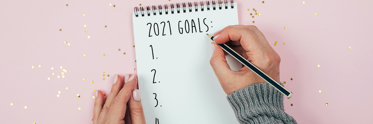 A woman writing on a pad surrounding by Glitter that says: 2021 Goals