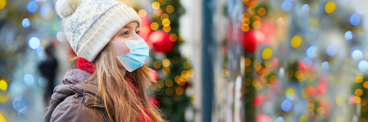 photo of woman in coronavirus mask looking at christmas decorations outside