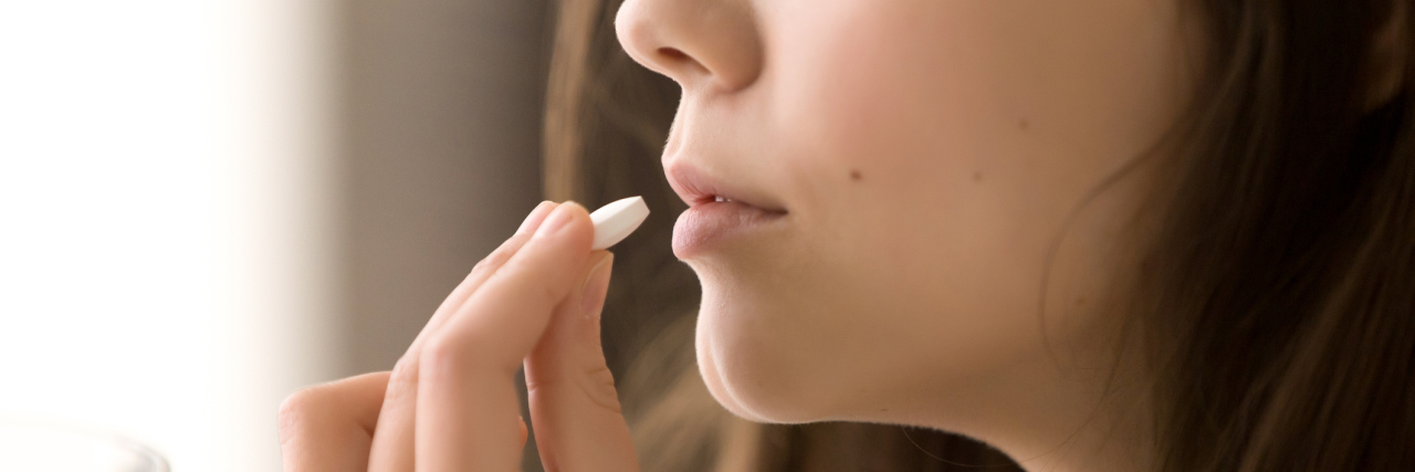 Why I Still Take Antidepressants, Even Though I'm Not Depressed photo close up of woman holding a white pill to her mouth and a glass of water in her hand