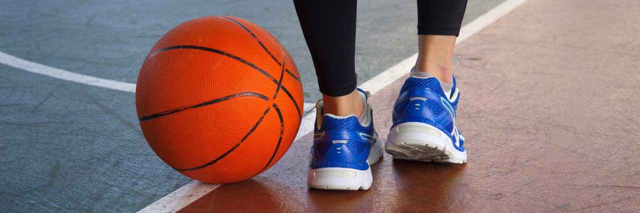 woman's blue sports shoes on a basketball court with a basketball next to her