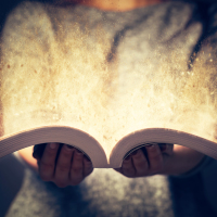 a woman holding open a book with light coming out of it
