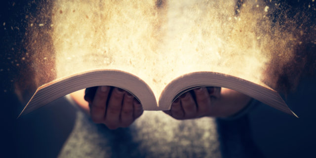 a woman holding open a book with light coming out of it