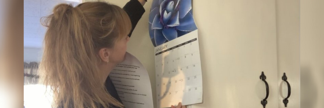 Breaking Up With January for My Mental Health A woman hanging up the calendar