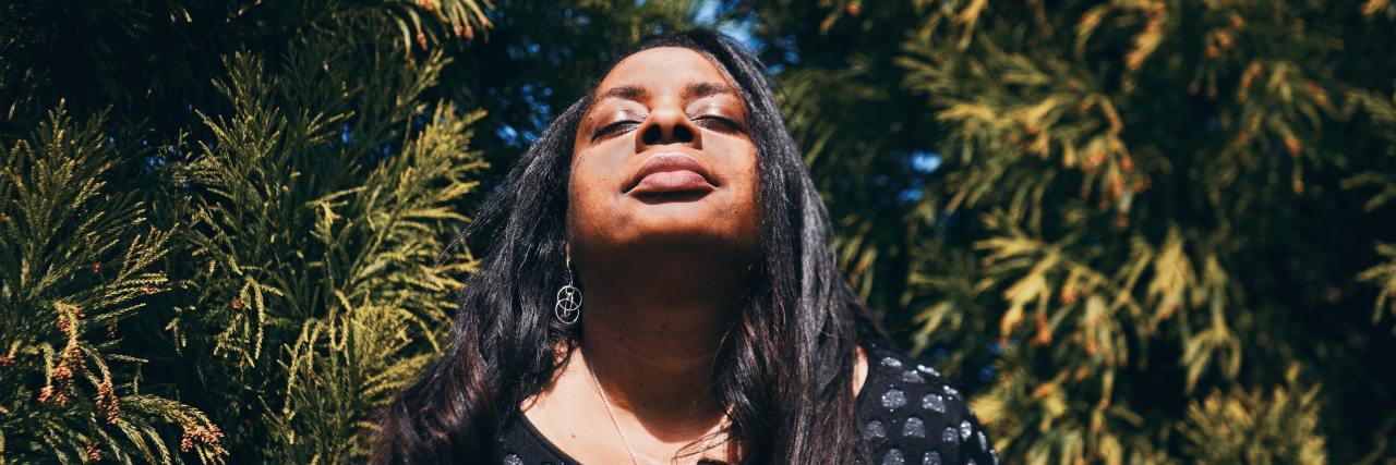 Whatever You're Feeling as 2020 Ends Is Valid woman with her eyes closed looking up with trees behind her