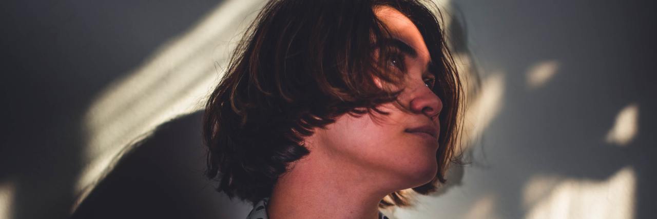 Reflections on COVID-19 From Somebody Housebound From Chronic Illness A woman in shadows looking up. She has short brown hair