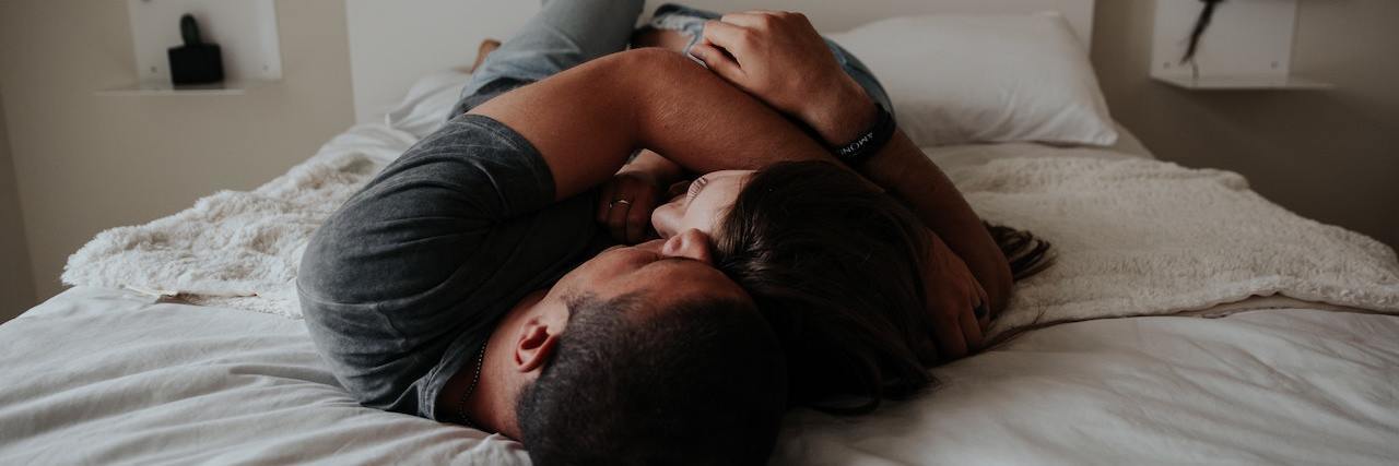 A Guide to Intimacy and Sex When Have Inflammatory Bowel Disease Two people cuddle close on a bed with a white sheet